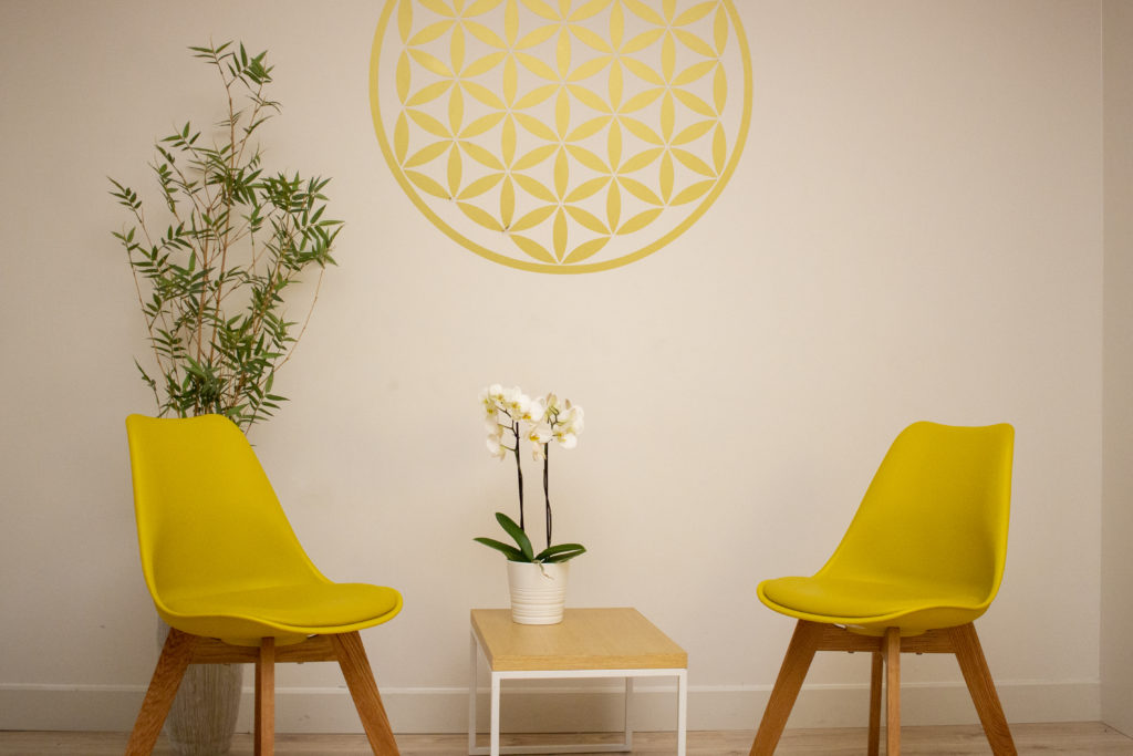 Lugar en el que se realiza las sesiones de terapia. Se ven dos sillas vacías con una flor de la vida en la pared en grande.